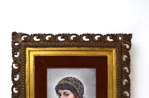 A miniature portrait of a young woman on a light-colored background in a red, gold, and brown ornate frame.